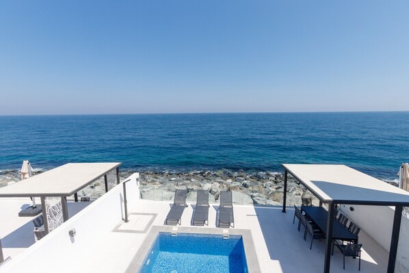 A rooftop pool with a view of the sea, lounge chairs, and a table.