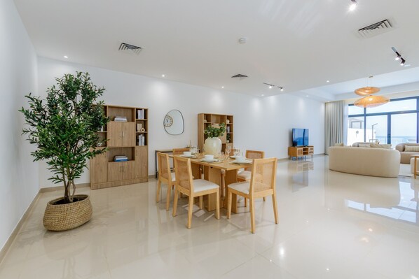 A modern living room with a dining area, a large potted plant, and a sofa.