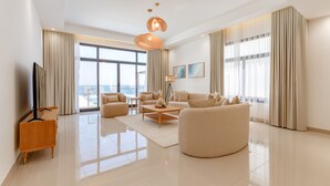 A spacious living room with a large window, a flat-screen TV, a coffee table, and a sofa. - Arabian Gulf-Facing 4BR Villa with Two Assistant Room, Heated Pool and Barbecue Space, Al Dana Island, Fujairah (Fujairah)