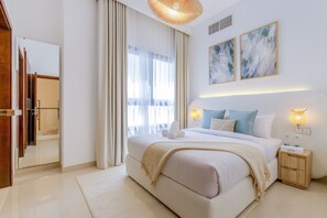 A modern hotel room with a large bed, a bedside table with a lamp, and a view of the city through the window.