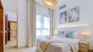 A modern hotel room with a large bed, a bedside table with a lamp, and a view of the city through the window. - Arabian Gulf-Facing 4BR Villa with Two Assistant Room, Heated Pool and Barbecue Space, Al Dana Island, Fujairah (Fujairah)