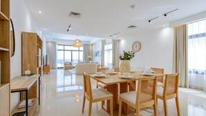 A modern dining area with a wooden table set for four, surrounded by wicker chairs. A large vase with a plant is on the table, and a clock is on the wall. - Arabian Gulf-Facing 4BR Villa with Two Assistant Room, Heated Pool and Barbecue Space, Al Dana Island, Fujairah (Fujairah)