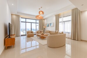 A spacious living room with a large window, a flat-screen TV, a coffee table, and a sofa.