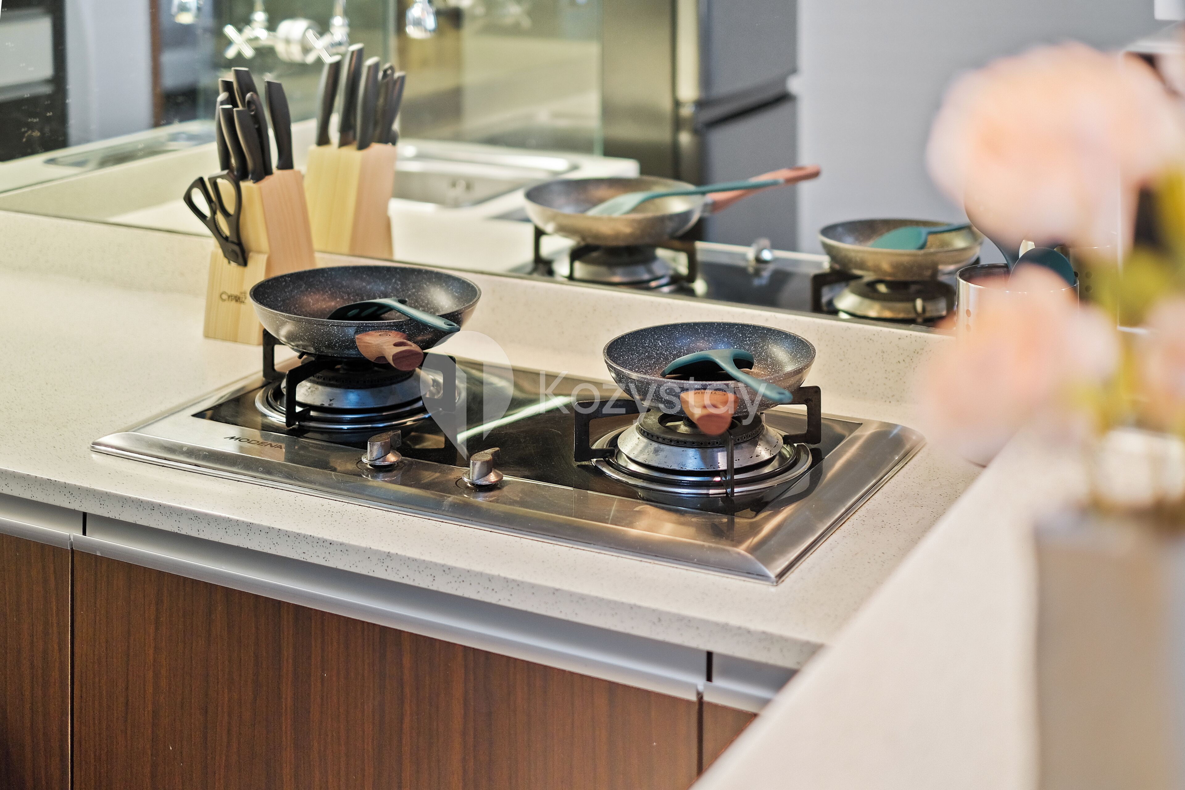 A kitchen with two gas stoves, a knife block, and a frying pan on the counter.