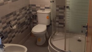 Baño con inodoro, bidé y ducha con mampara de vidrio.