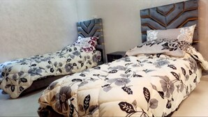 Dos camas individuales con ropa de cama estampada con motivos florales y cabeceros con diseños geométricos.