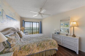 Une chambre à coucher avec un lit, une commode, un ventilateur de plafond, une fenêtre donnant sur un beau paysage et un tableau accroché au mur.