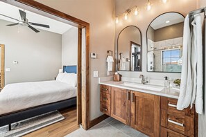Relax in this serene bedroom with a large bed and adjacent bathroom featuring a sink, mirror, and vanity.