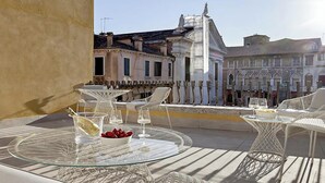 A balcony with glass tables and white wicker chairs, overlooking historic buildings with a statue. - Luxurious 300 sqm Apartment with Canal View in Cannaregio (Venezia)