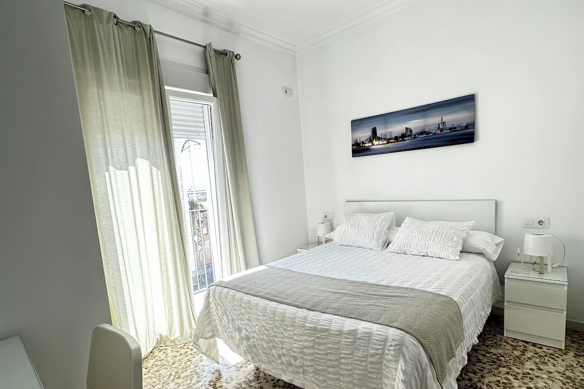 Une chambre d’hôtel avec un lit, une table de chevet, un bureau et une fenêtre avec des rideaux.