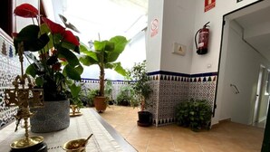 A room with a tiled floor, a table with a white tablecloth, potted plants, and a fire extinguisher on the wall. - Hostal Mellizo (Lebrija)