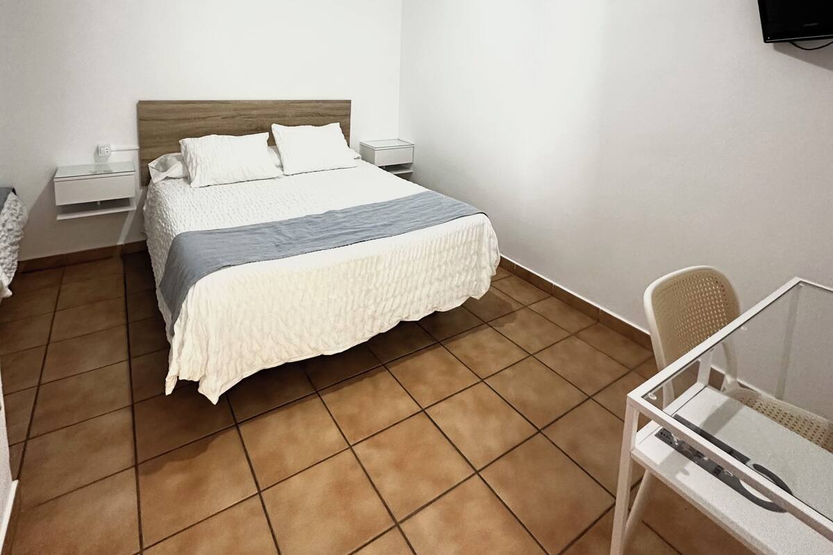 Une chambre d’hôtel avec un lit, des tables de chevet, une télévision, une chaise et une petite table.