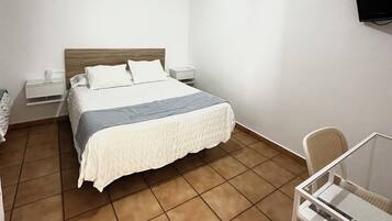 Una habitación de hotel con una cama, mesitas de noche, un televisor, una silla y una pequeña mesa.