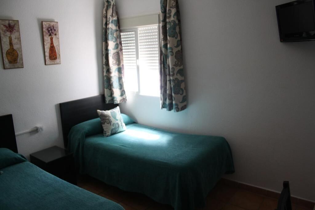 Una habitación con dos camas individuales, una ventana con cortinas, un televisor de pantalla plana montado en la pared y obras de arte en la pared.