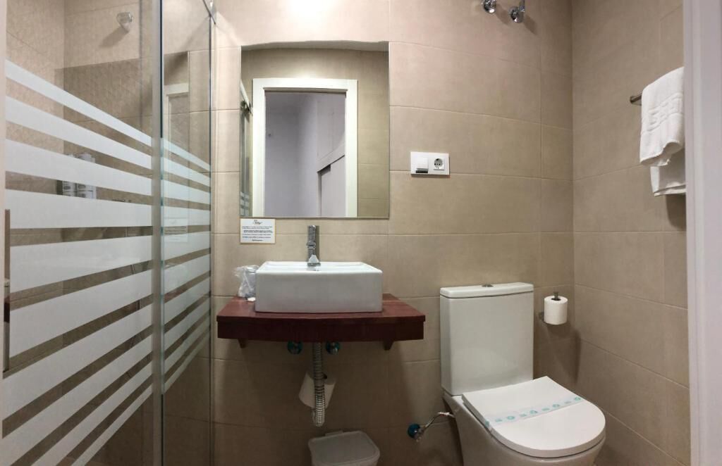 Ein Badezimmer mit Duschkabine aus Glas, einem weißen Waschbecken mit Spiegel darüber, einer Toilette und einem Handtuchhalter.