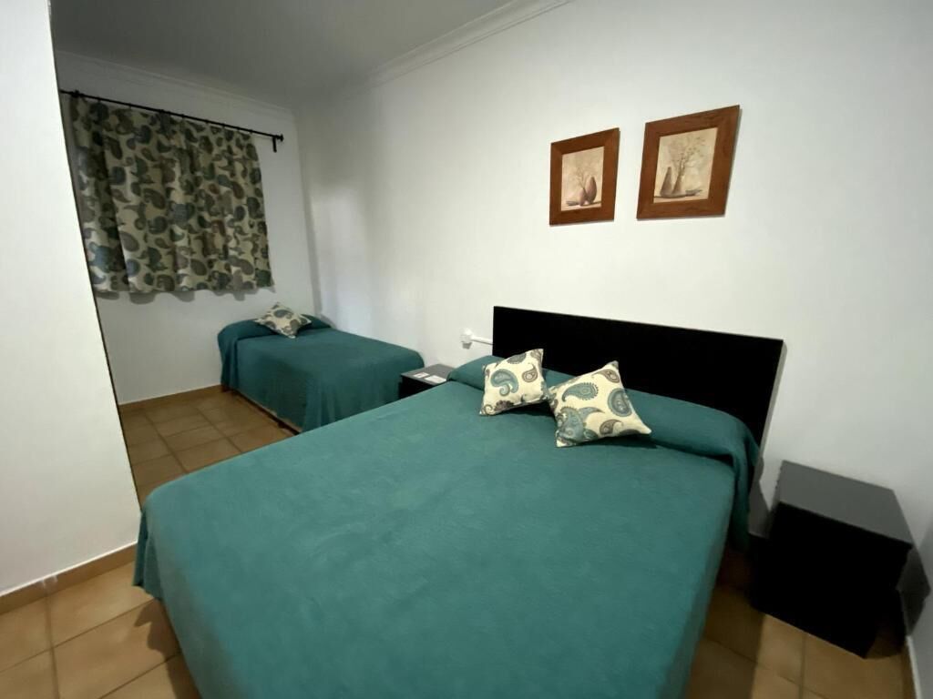 Een kamer met twee bedden, elk met blauwgroene beddengoed en geborduurde kussens, een klein nachtkastje en een aan de muur bevestigde televisie.