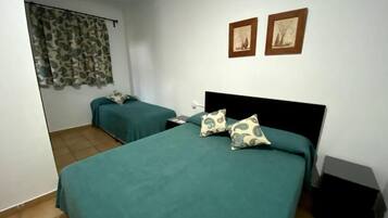 Een kamer met twee bedden, elk met blauwgroene beddengoed en geborduurde kussens, een klein nachtkastje en een aan de muur bevestigde televisie.