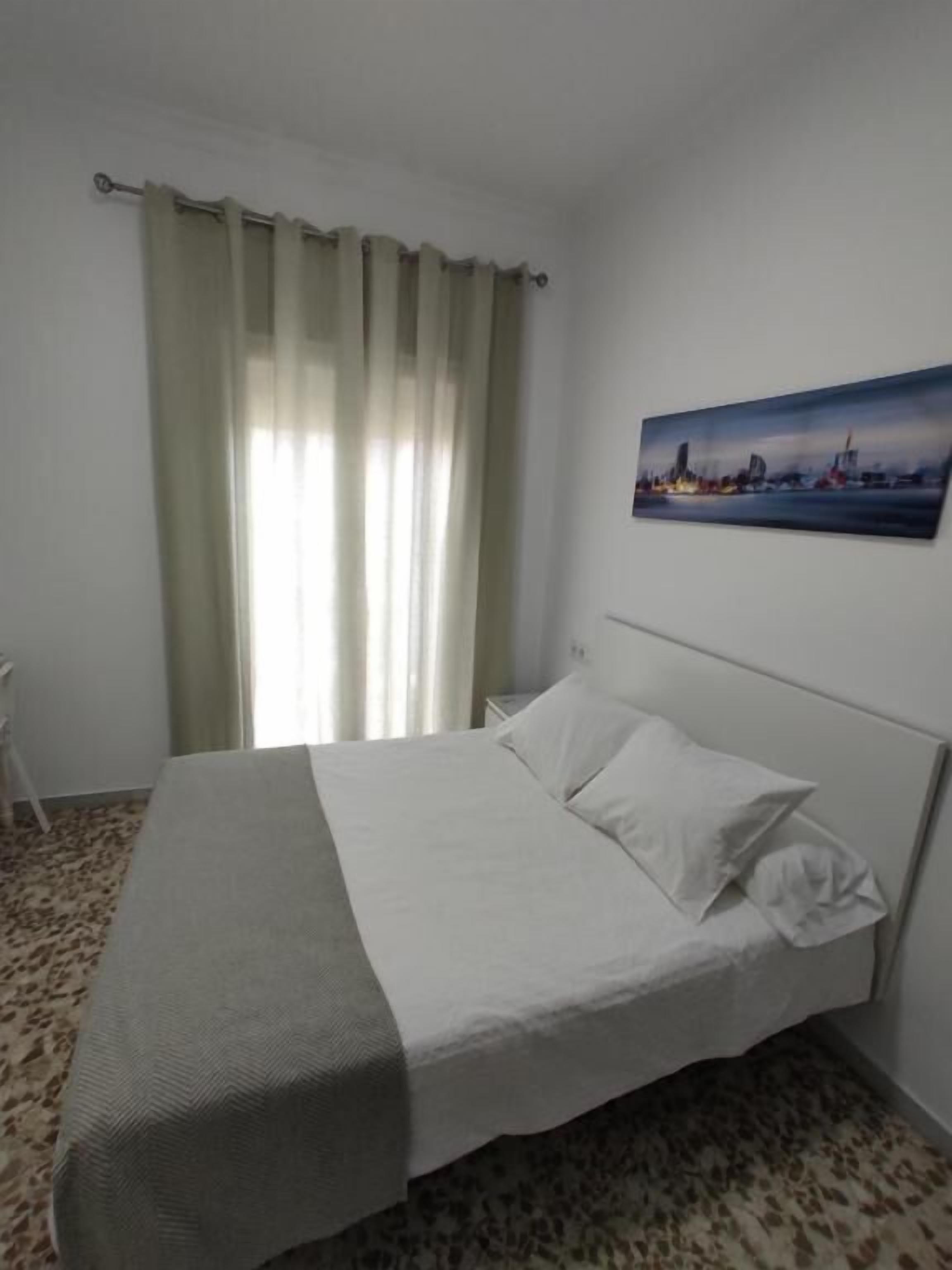 Une chambre d’hôtel avec un lit, un tableau au mur et une fenêtre avec des rideaux.