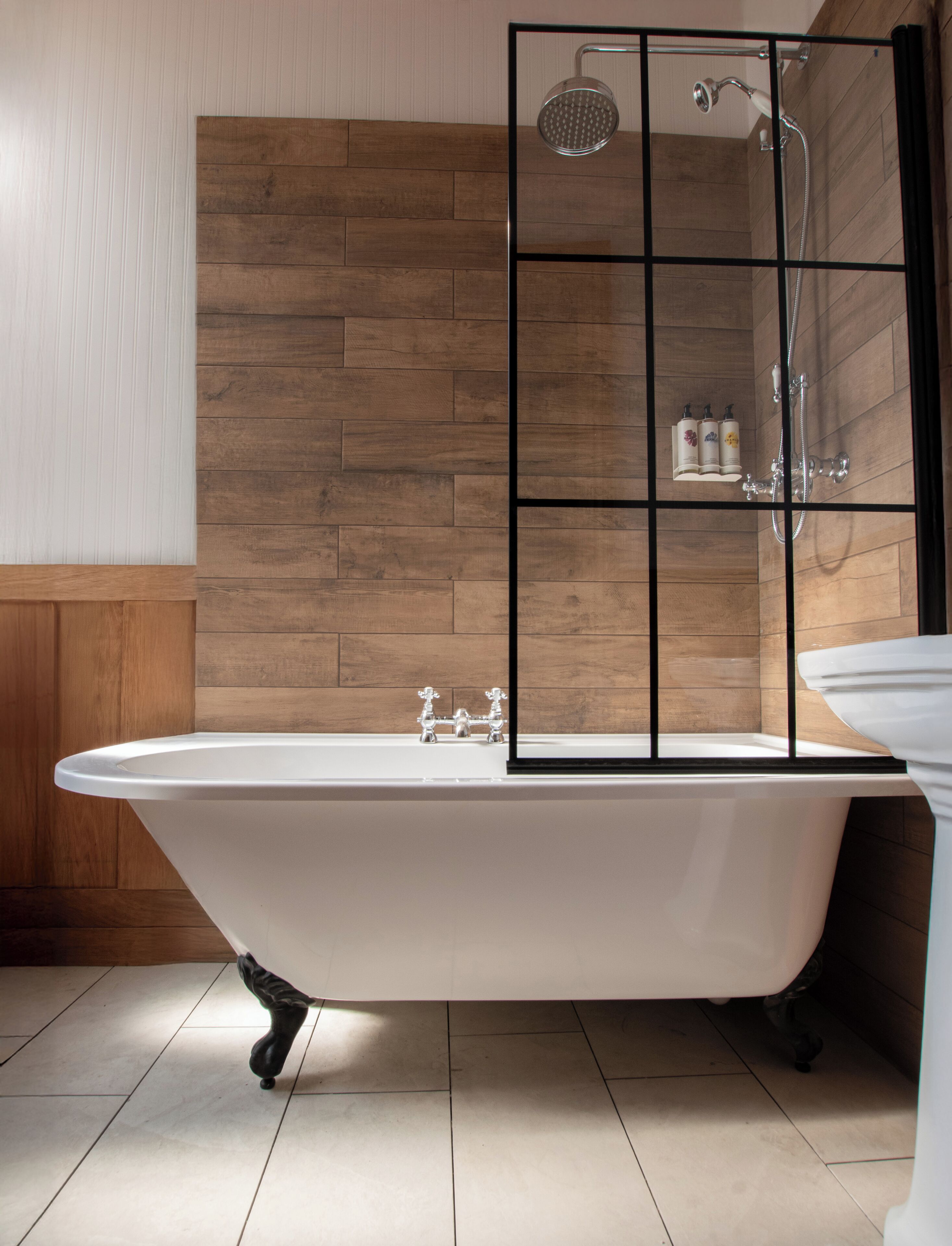 A bathroom with a freestanding bathtub, a shower enclosure, and a wooden panel wall.