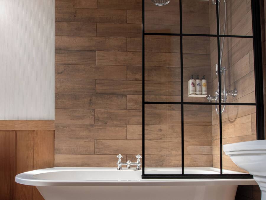A bathroom with a freestanding bathtub, a shower enclosure, and a wooden panel wall.