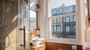 Une salle de bain avec un meuble-lavabo en bois, un évier, un miroir et une fenêtre donnant sur un immeuble.