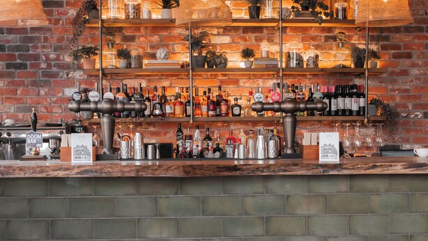 Un espace bar avec des chaises en bois, un mur en briques et des étagères remplies de bouteilles et de verres.