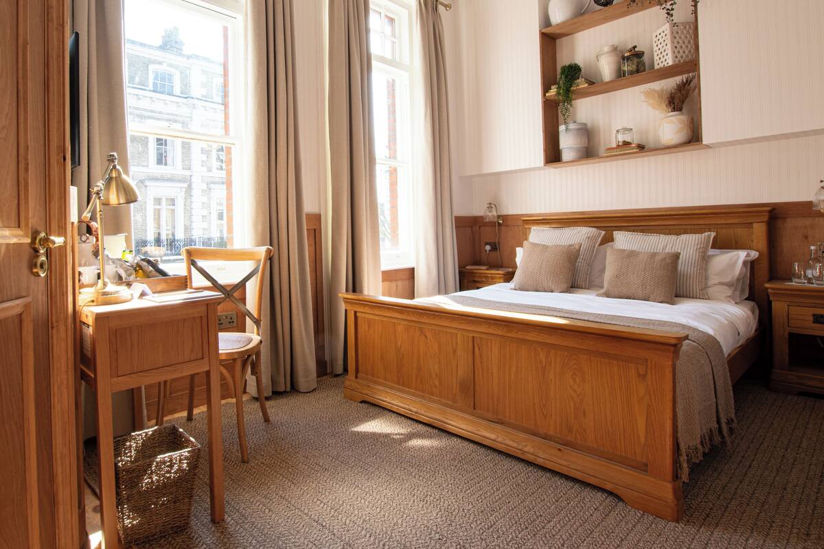 Une chambre à coucher avec un lit en bois, un bureau avec une chaise, une table de chevet et une étagère ornée d’objets décoratifs.