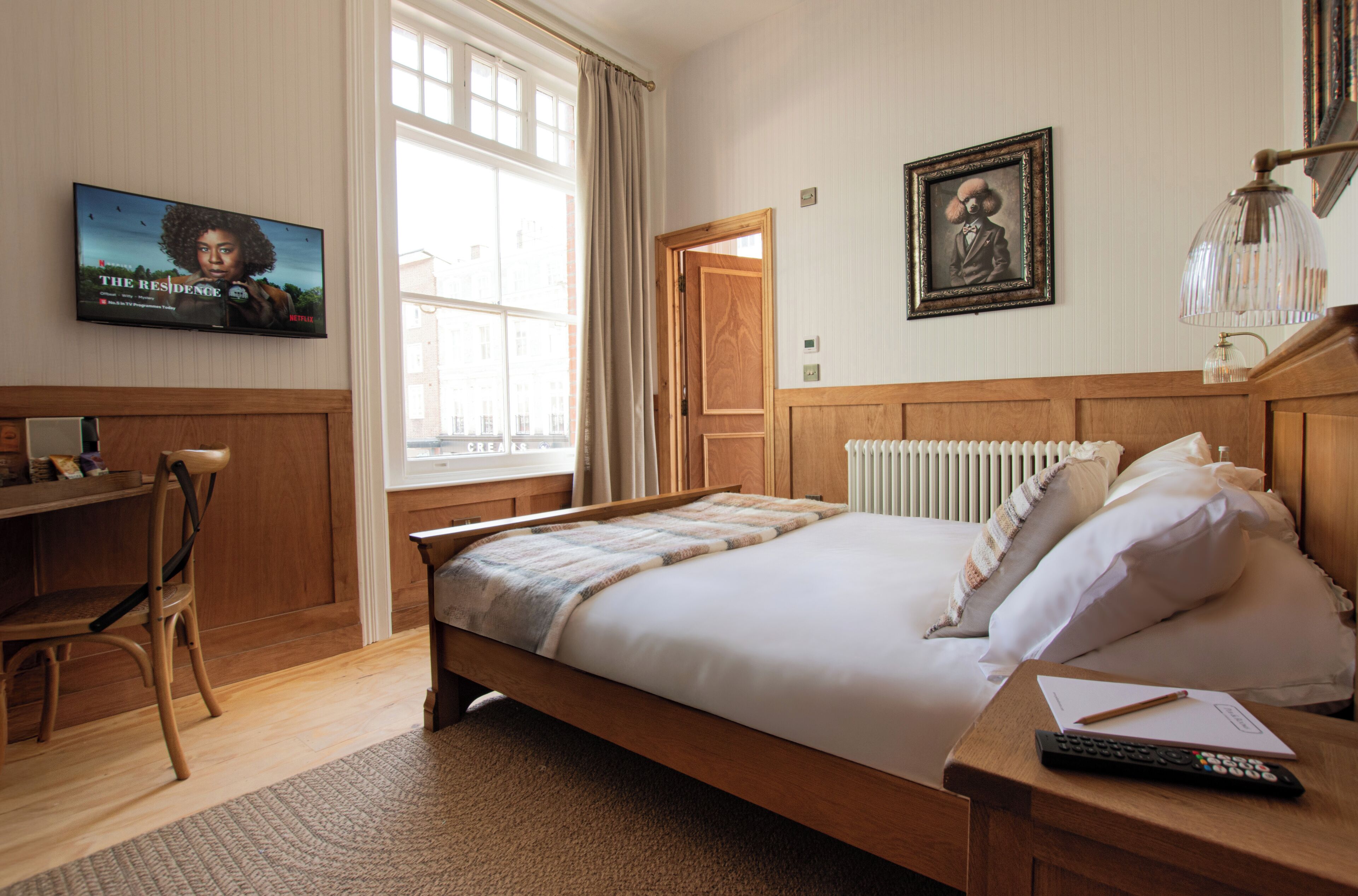 Een slaapkamer met een houten bed, een bureau, een stoel, een televisie en een raam met gordijnen.