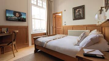 A bedroom with a wooden bed, a desk, a chair, a television, and a window with curtains.