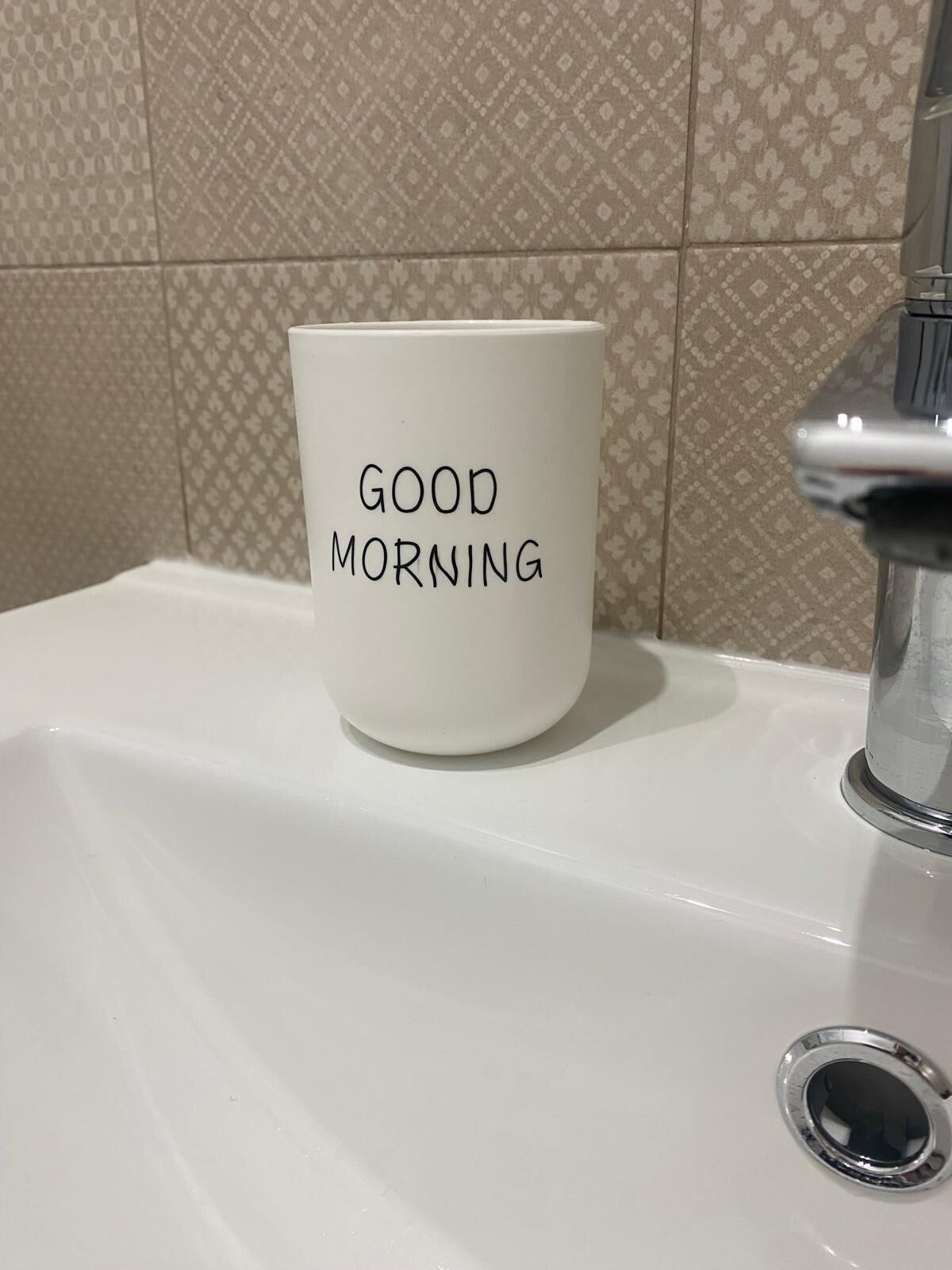 Eine weiße Tasse mit der Aufschrift "GOOD MORNING" auf einem weißen Waschbecken.