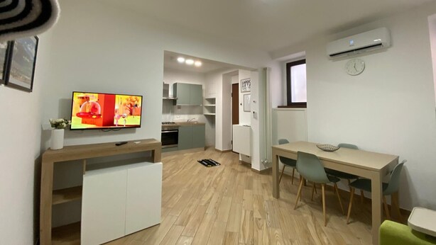 Un espace de vie compact comprenant un coin cuisine, un coin repas et un téléviseur fixé au mur.