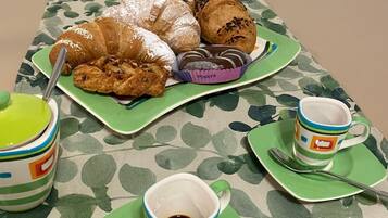 A table with pastries, coffee cups, and spoons on a patterned tablecloth.
