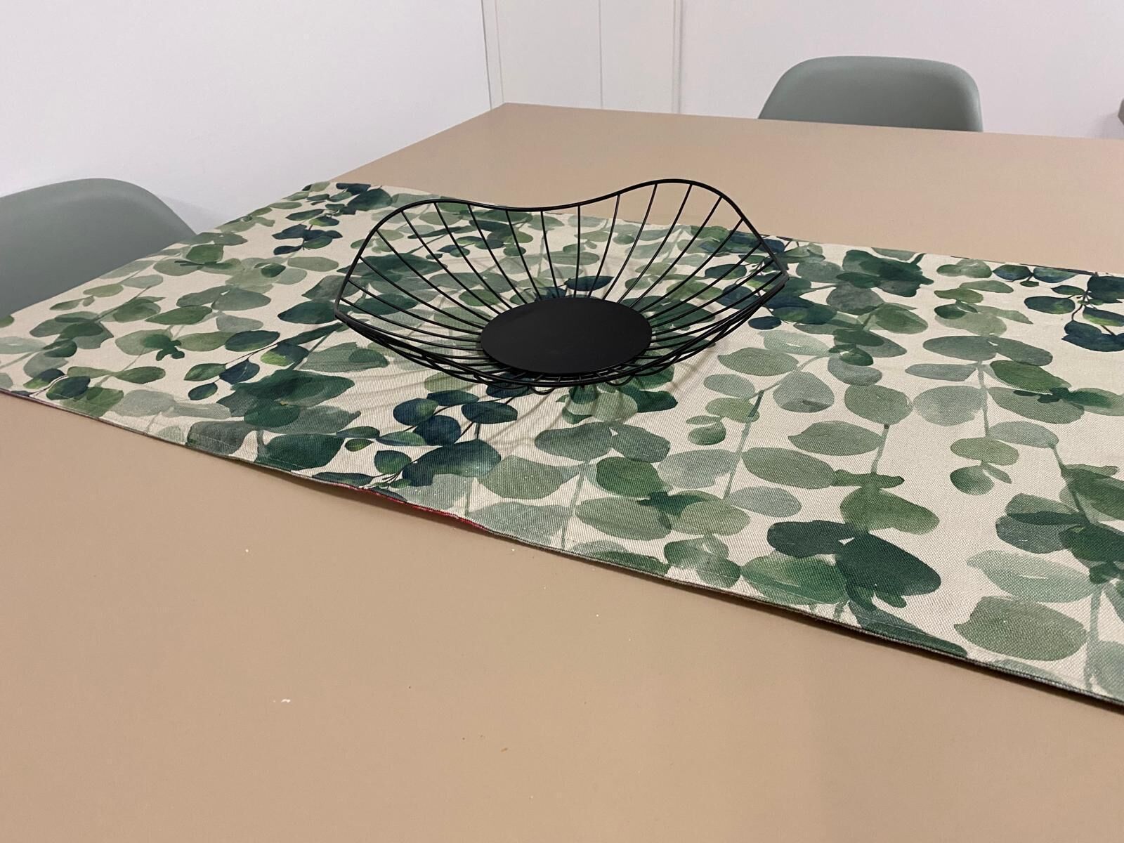 A table with a leaf-patterned tablecloth and a black wire bowl on it.