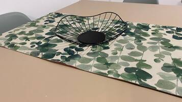 A table with a leaf-patterned tablecloth and a black wire bowl on it.