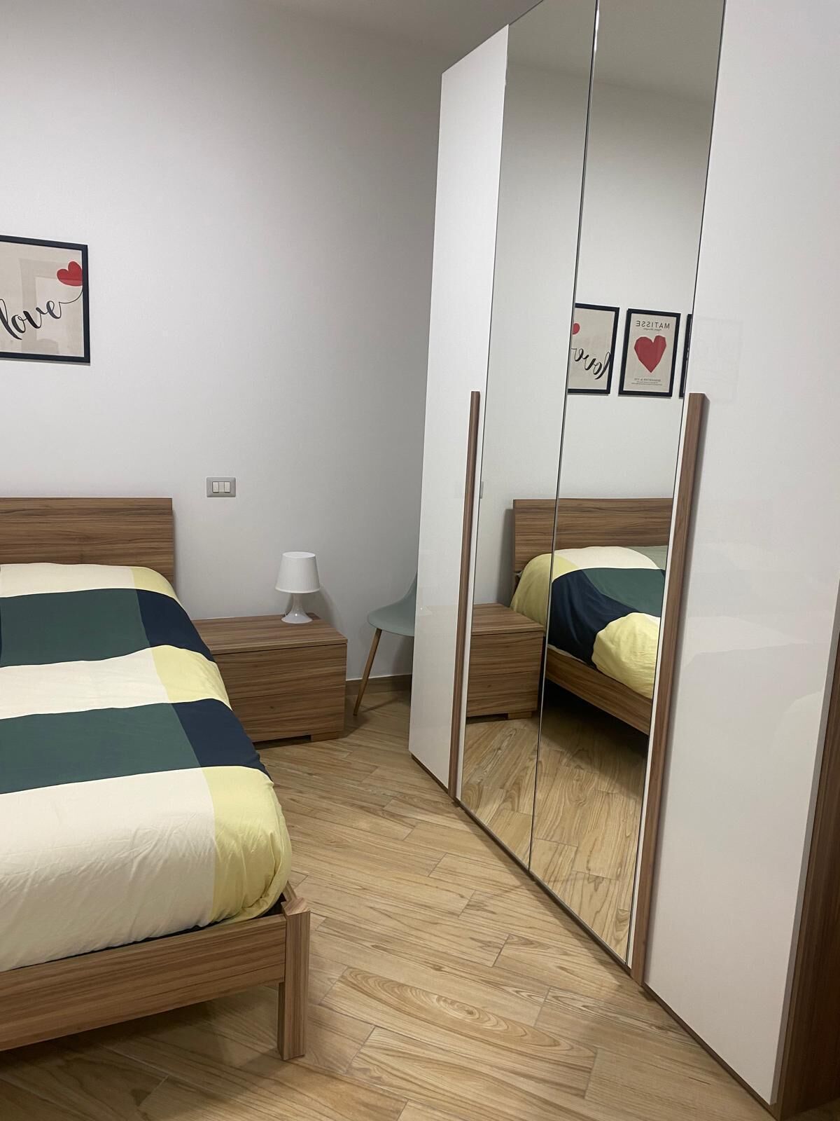 A bedroom with a bed, bedside table, lamp, and a large mirror.