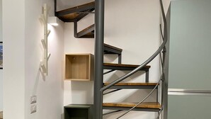 Un escalier en colimaçon avec des marches en bois et des rampes en métal, menant à un palier doté d’étagères intégrées.