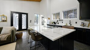 Una cocina moderna con una isla grande, armarios oscuros y techo de madera.