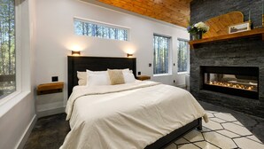Un dormitorio con una cama grande, una chimenea de piedra y dos ventanas.