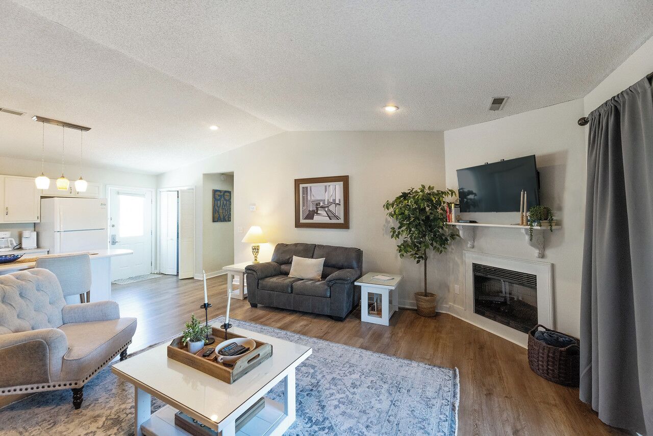 A modern living room with a sofa, coffee table, and a fireplace. There is a television mounted on the wall and a plant in the corner.