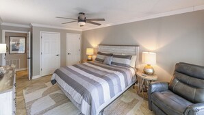 Ein Schlafzimmer mit einem Bett, zwei Nachttischlampen, einem Deckenventilator, einem Ledersessel und einer Tür zu einem anderen Raum.