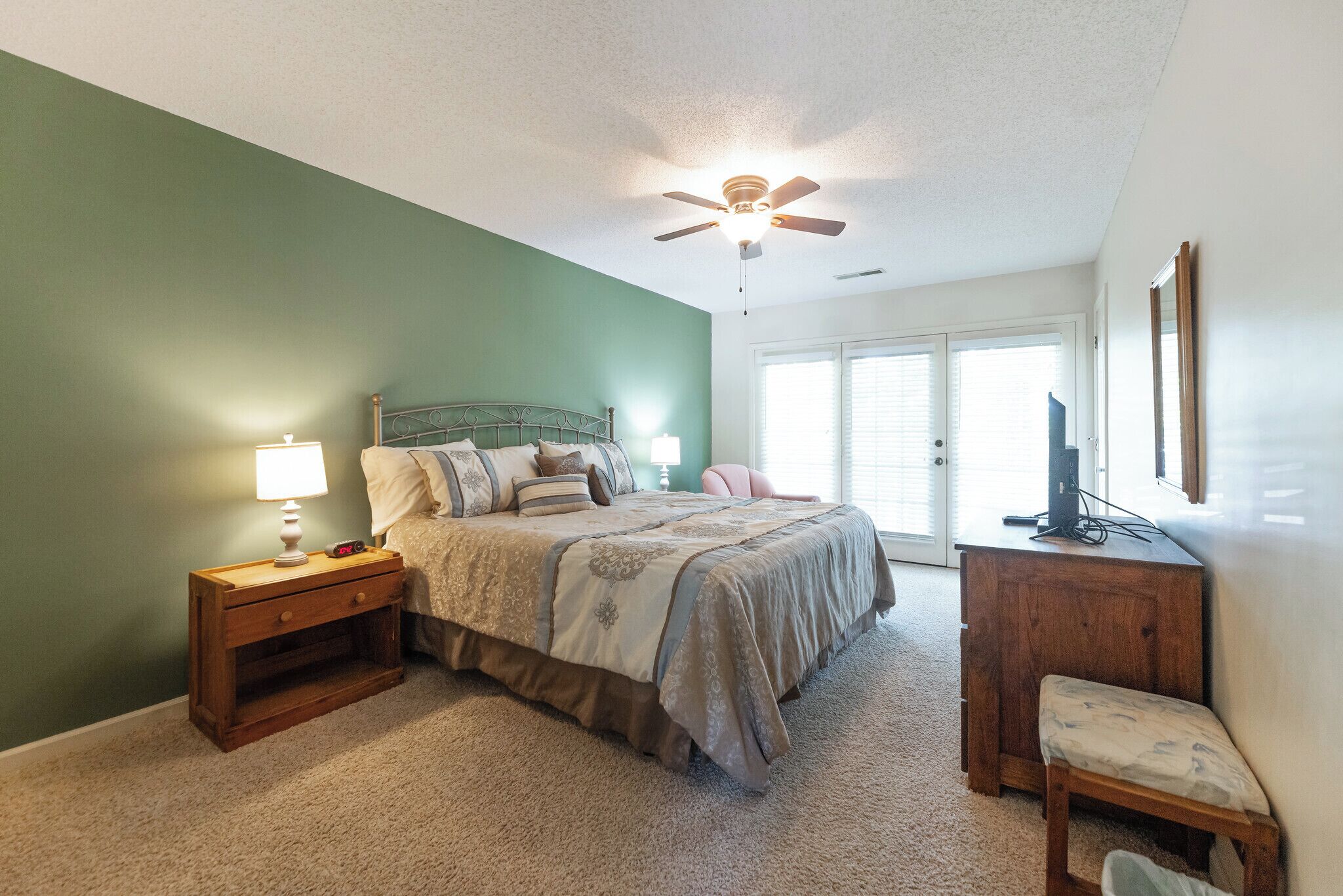 A bedroom with a bed, nightstand, chair, and a ceiling fan.