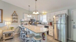 Una cocina moderna con armarios blancos, un refrigerador de acero inoxidable, una encimera de granito y taburetes de bar.