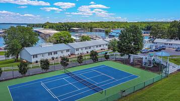 A tennis court surrounded by a fence, with a building and trees nearby.