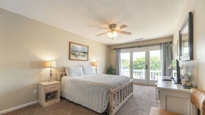 A bedroom with a bed, nightstands, a desk, a chair, a ceiling fan, and a large window with a view of greenery. - One Bedroom Harbor View Condo (Grand Rivers)