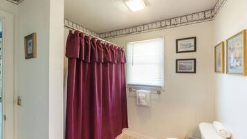 Un baño con inodoro blanco, cortina de ducha y una ventana con persianas.