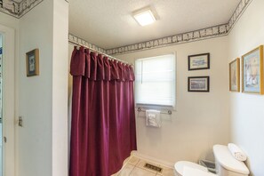 A bathroom with a white toilet, a shower curtain, and a window with blinds. - One Bedroom Harbor View Condo (Grand Rivers)