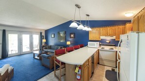 A compact kitchen with wooden cabinets, a central island, a microwave, and a refrigerator. - One Bedroom Harbor View Condo (Grand Rivers)