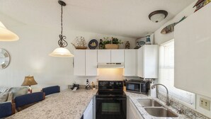 A compact kitchen with white cabinets, a black stove, and a granite countertop. - One Bedroom Harbor View Condo (Grand Rivers)