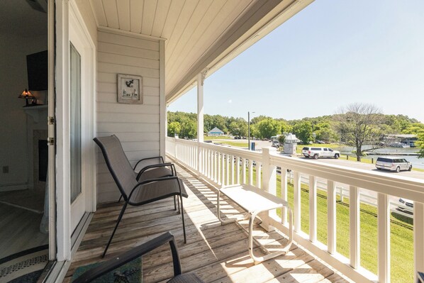 A covered porch with two chairs and a bench, overlooking a road with vehicles and a green landscape.