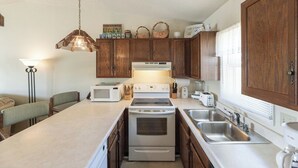 Une cuisine compacte dotée de meubles en bois, d’un four à micro-ondes, d’un four traditionnel, d’un évier et d’un coin repas avec des chaises.